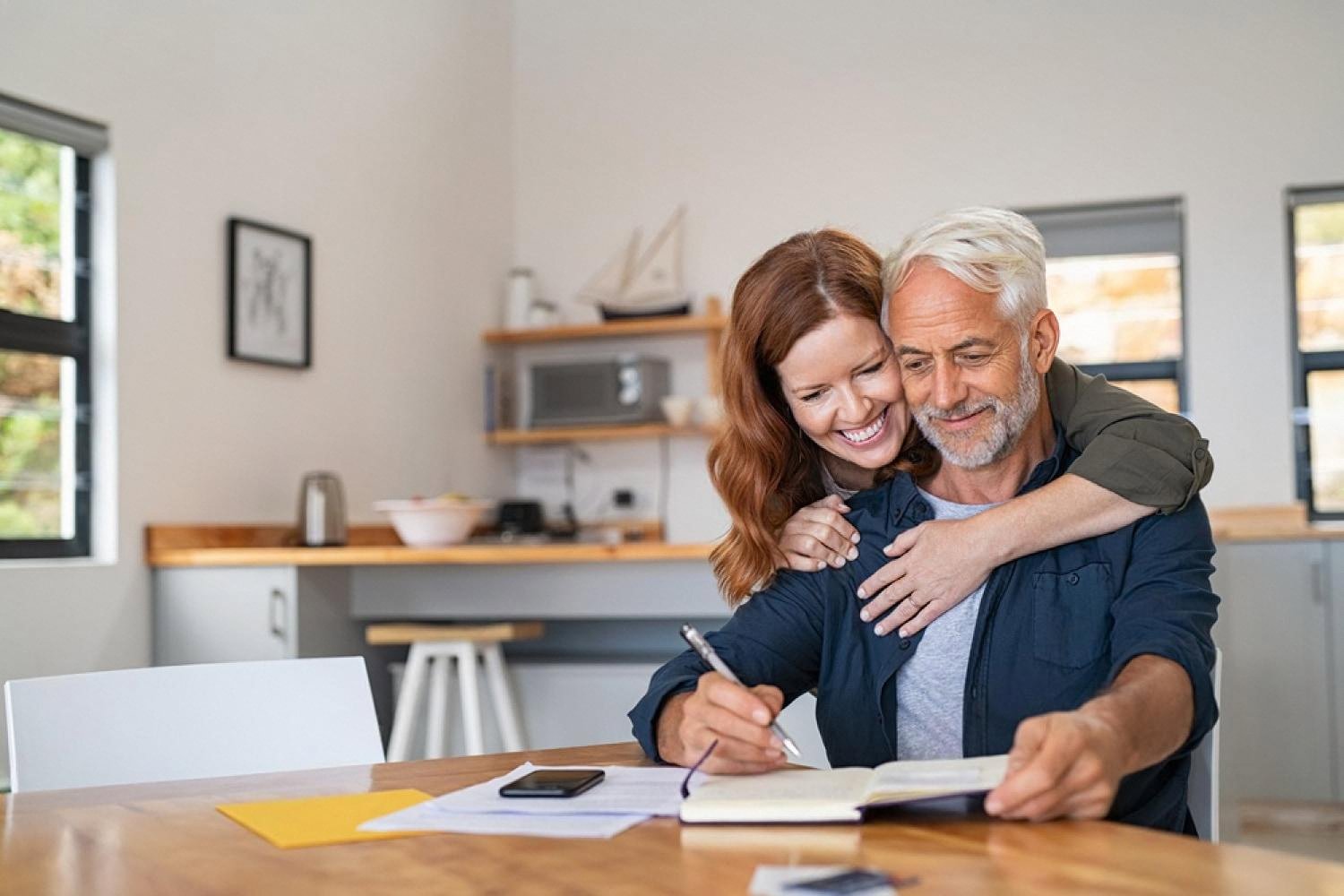 Smiling couple writing down a household budget and future financial plan together at a kitchen table
