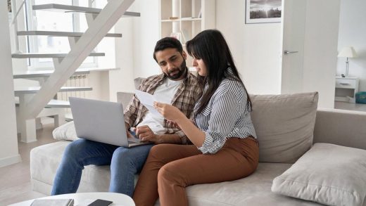 Young couple in a UAE apartment reviewing bills and financial documents on a laptop